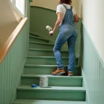 Femme peignant un escalier en bois en vert sauge sans ponçage dans un appartement rénové