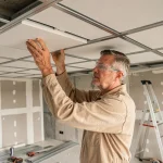 Artisan en train de poser un faux plafond suspendu dans une pièce en rénovation, illustration du coût de main-d'œuvre au m²